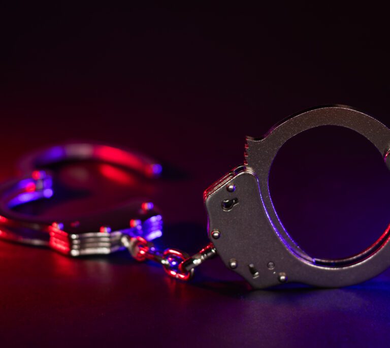 A pair of metal handcuffs is placed on a dark surface, illuminated by red and blue lights—symbolizing the urgency to contact a meth arrest lawyer Dayton if you find yourself in trouble.