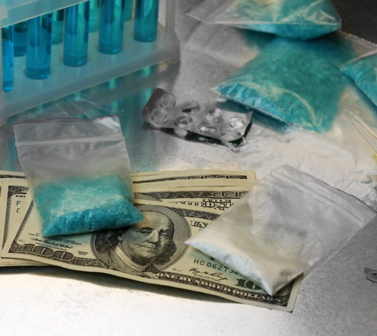 Bags of blue and white powder, syringes, test tubes, blister packs, and US dollar bills arranged on a metallic surface suggest the scene of a methamphetamine charge near Dayton.